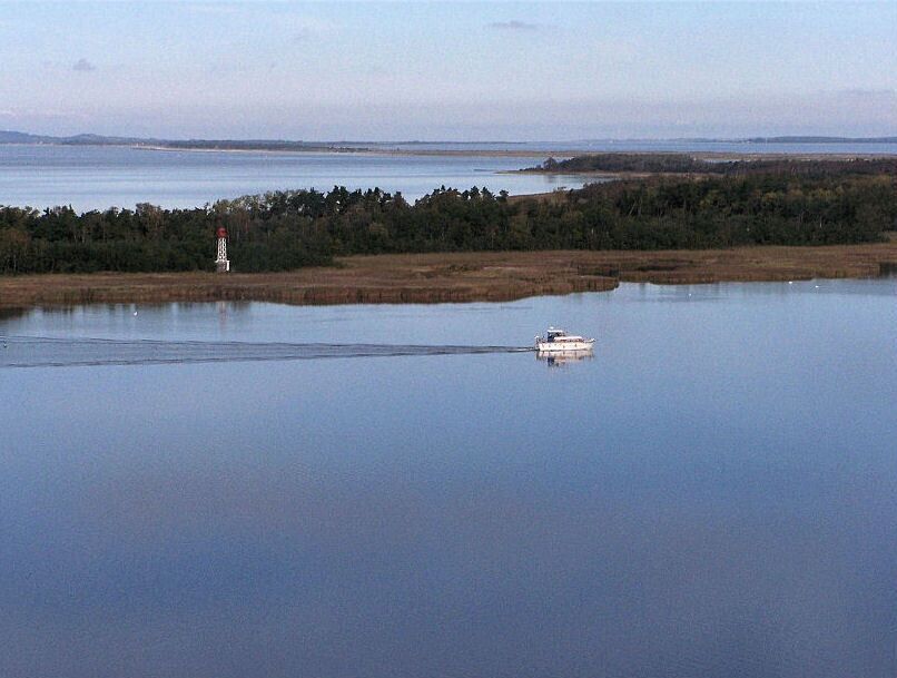 A calm lake with a boat and a lighthouse in the distance.