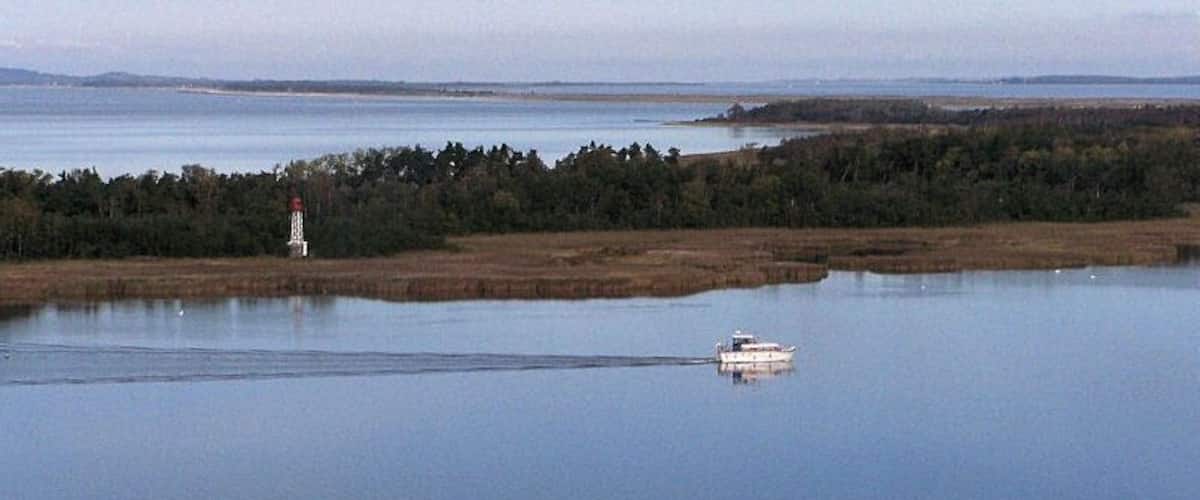 A calm lake with a boat and a lighthouse in the distance.