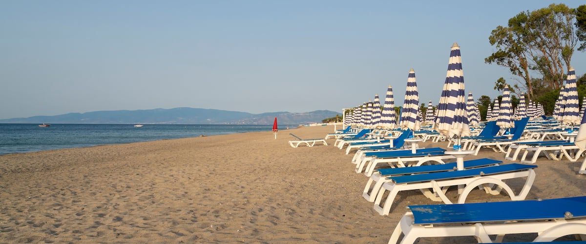 Blue and white umbrella and beach chairs at the beach in front of blue sea and blue sky. Calabria, Simeri Mare, Italy.
