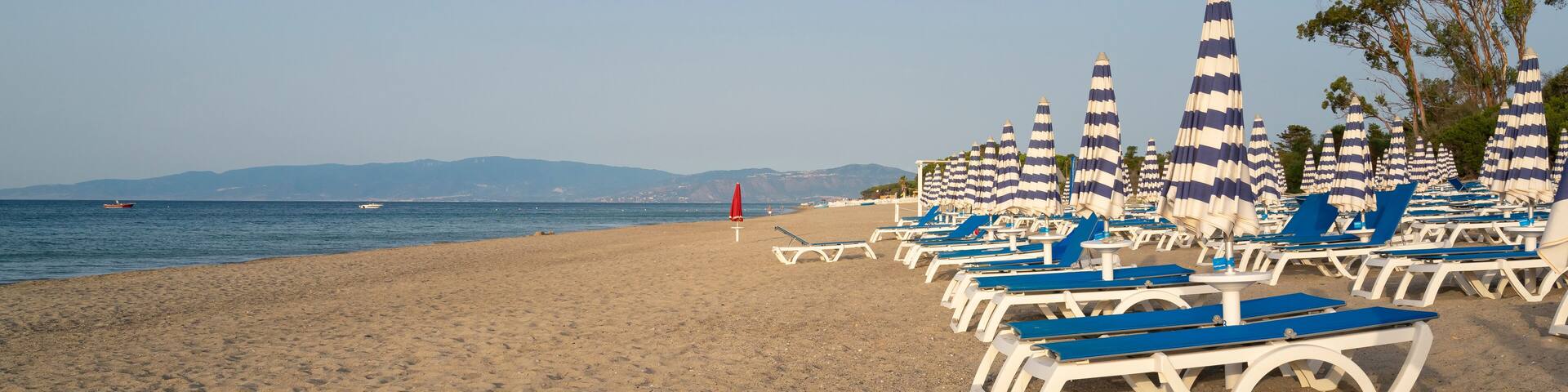 Blue and white umbrella and beach chairs at the beach in front of blue sea and blue sky. Calabria, Simeri Mare, Italy.