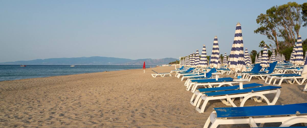 A beach with rows of blue and white striped beach umbrellas and lounge chairs.
