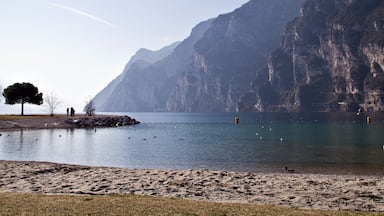 A calm lake with a sandy beach, a few people, and a large mountain in the background.