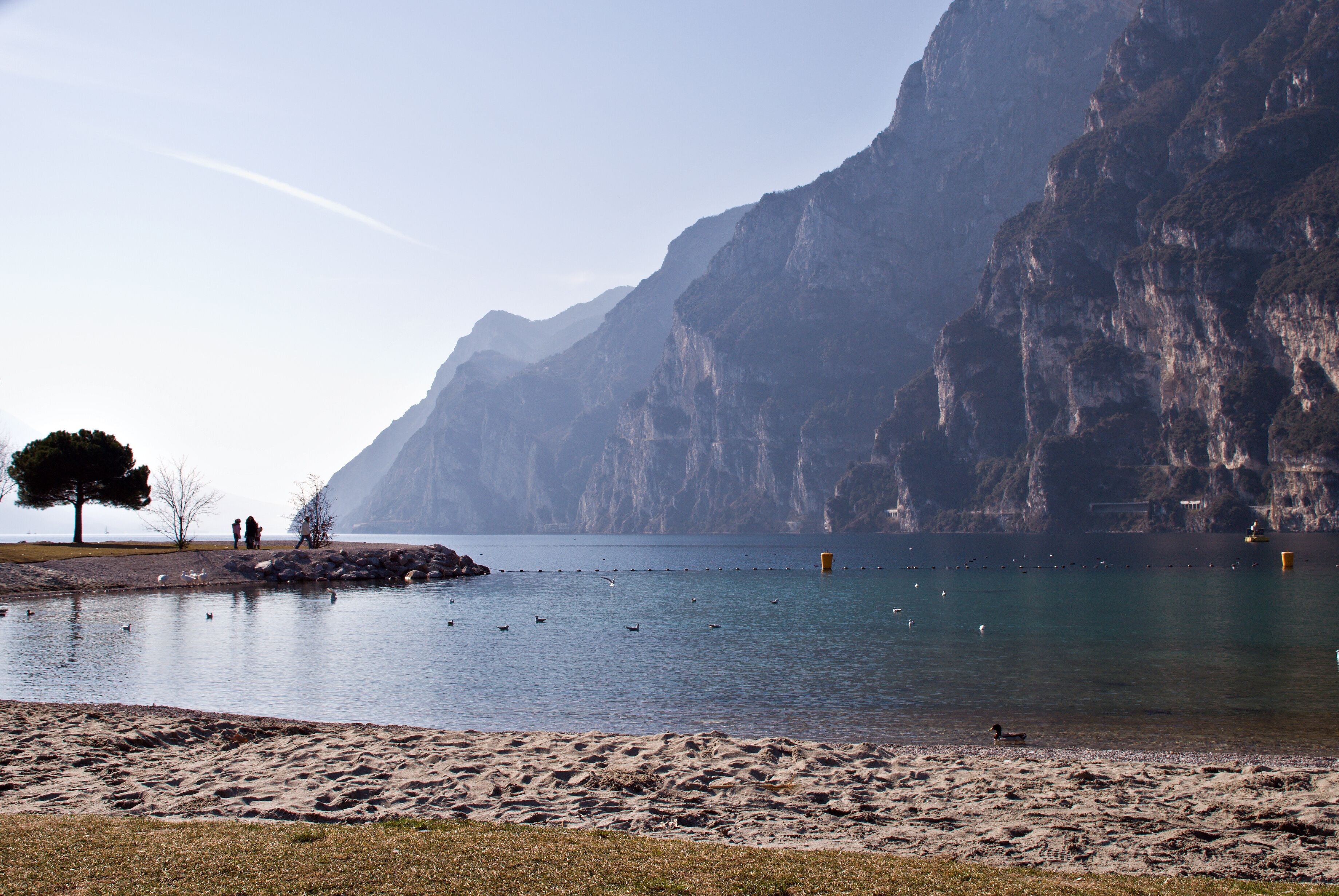 A calm lake with a sandy beach, a few people, and a large mountain in the background.
