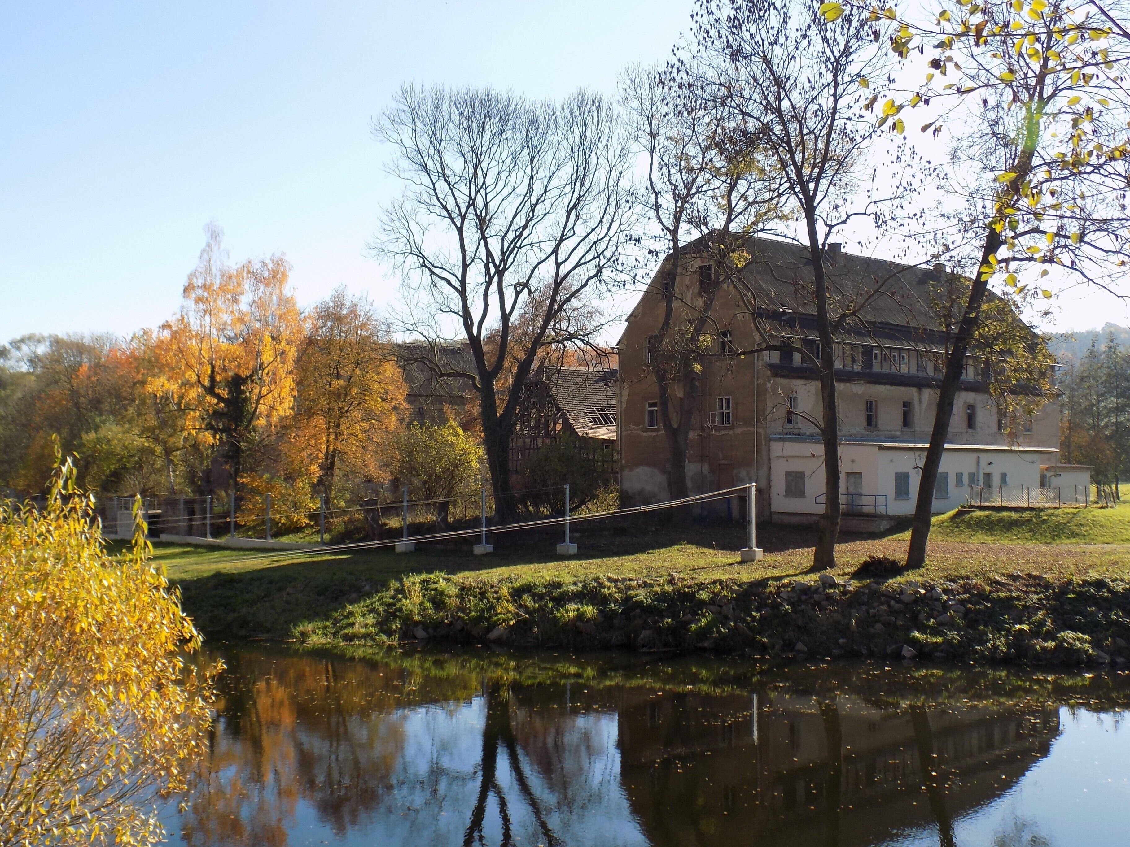 A historic building with a large pond in front, surrounded by autumn trees.