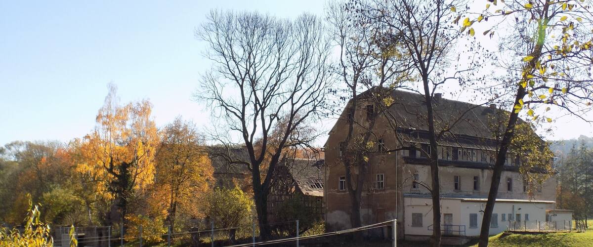 A historic building with a large pond in front, surrounded by autumn trees.