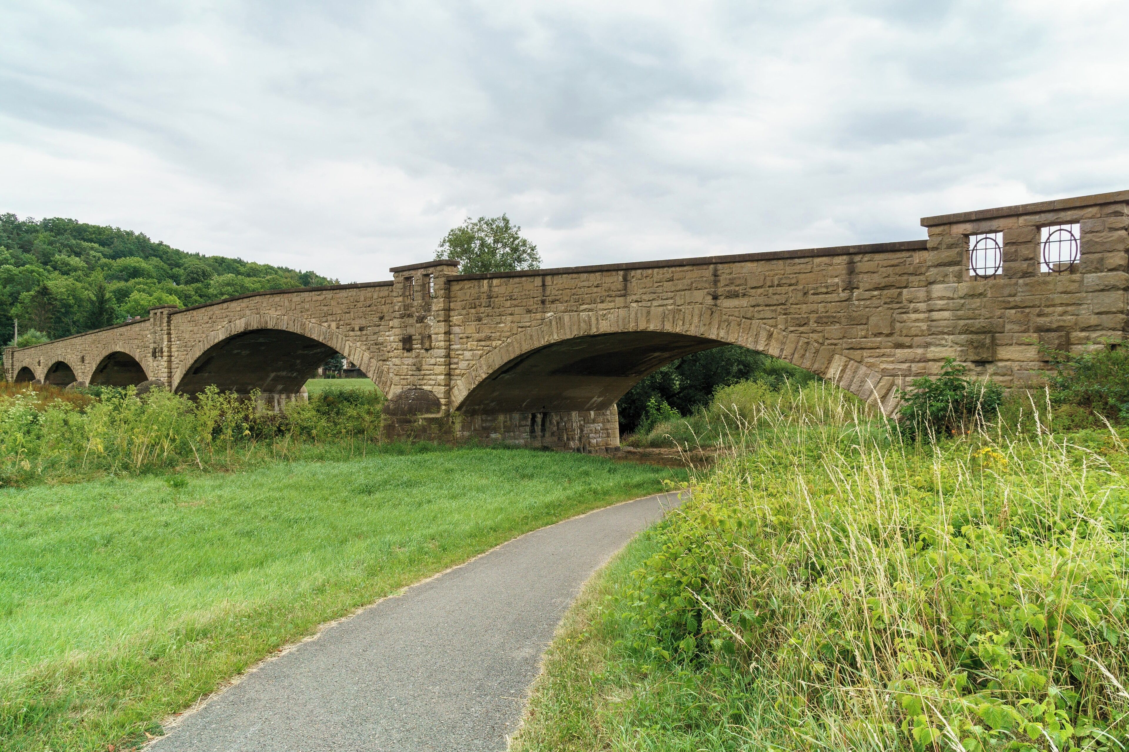 A stone bridge with multiple arches over a paved path.