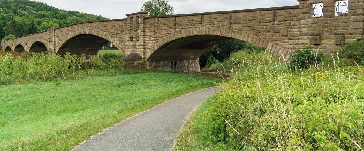 A stone bridge with multiple arches over a paved path.