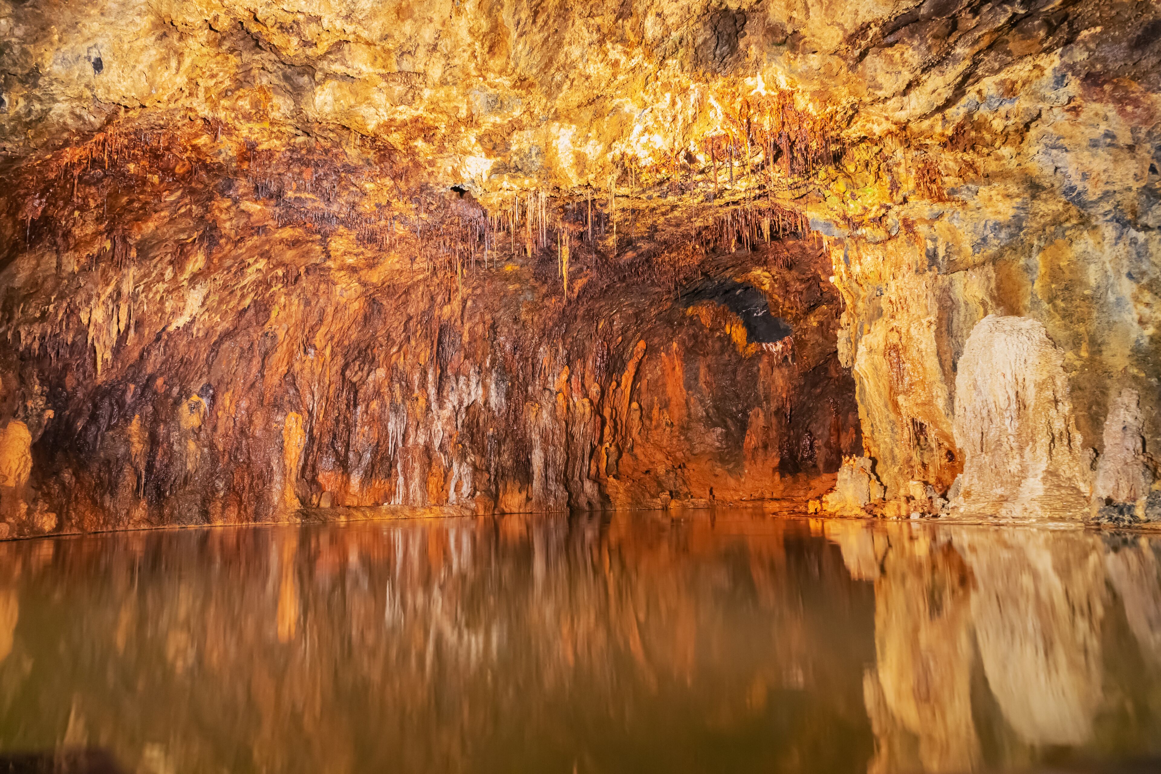 A cave with stalactites and stalagmites, a reflective pool, and a cave entrance.