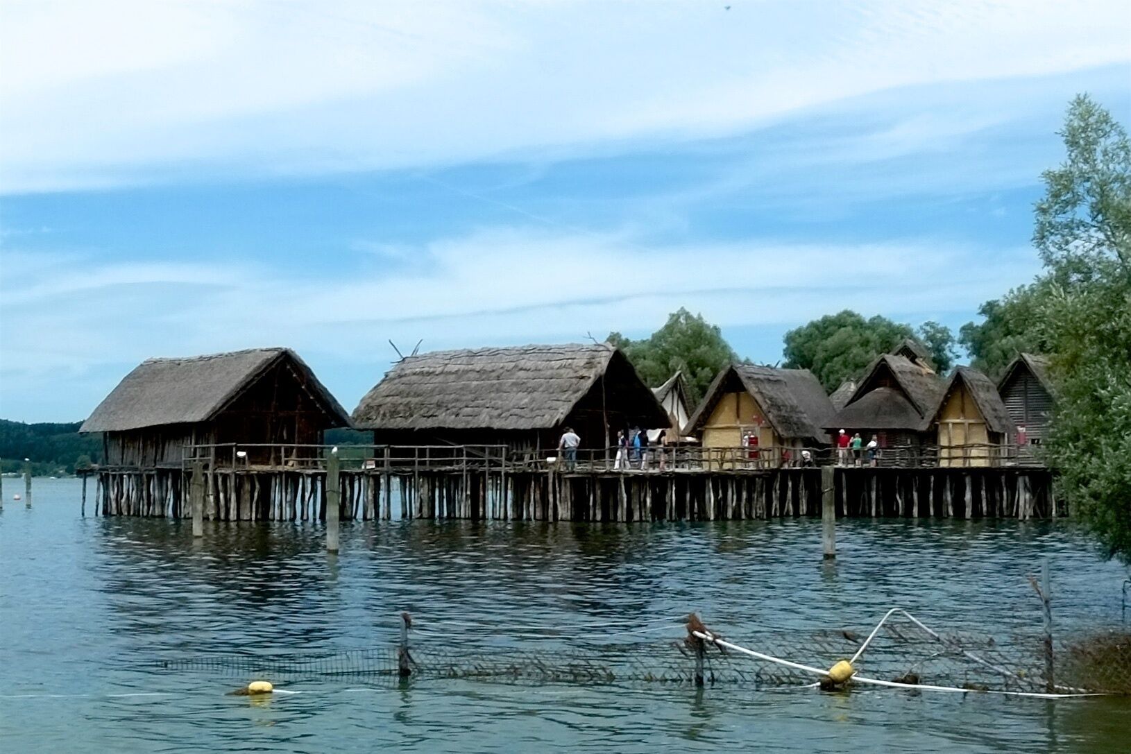 Thatched-roof huts on stilts over water, surrounded by trees.