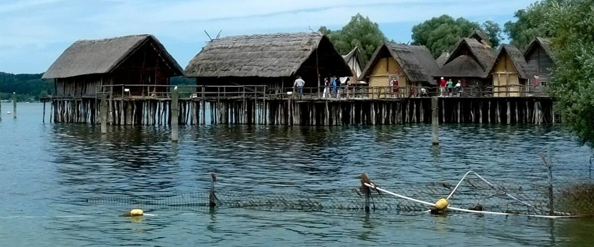 Thatched-roof huts on stilts over water, surrounded by trees.