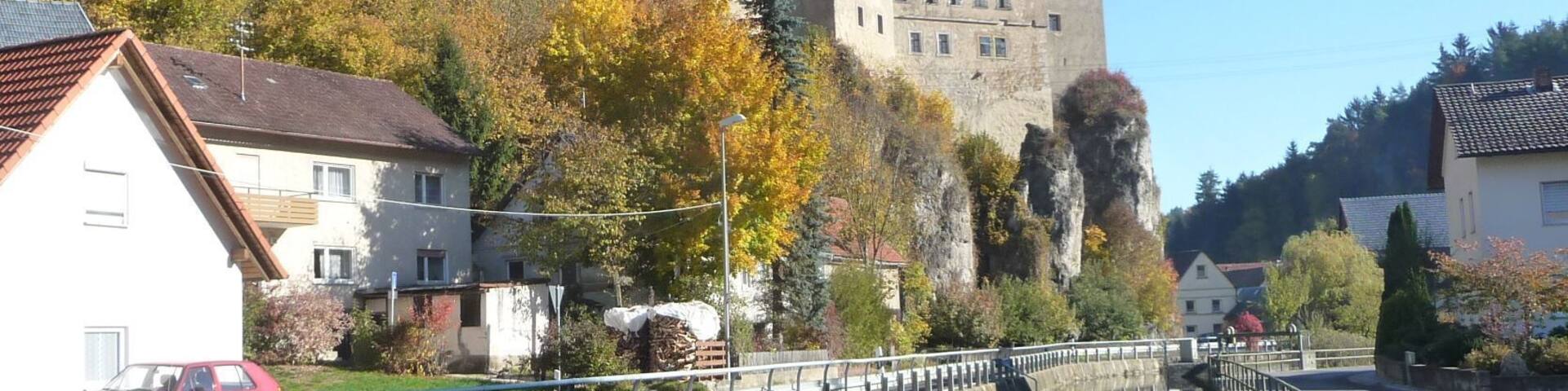 A castle on a hill, a canal with a bridge, and autumn-colored trees.