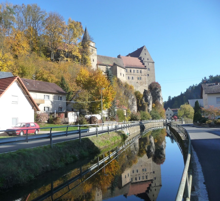 A castle on a hill, a canal with a bridge, and autumn-colored trees.
