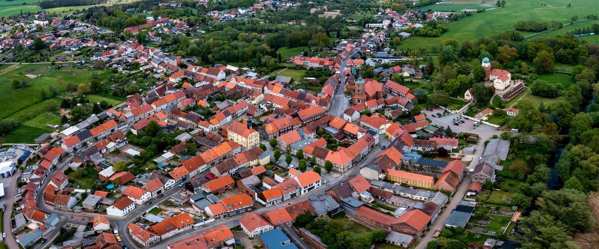 An aerial view of a town with red-roofed buildings, green fields, and a river.