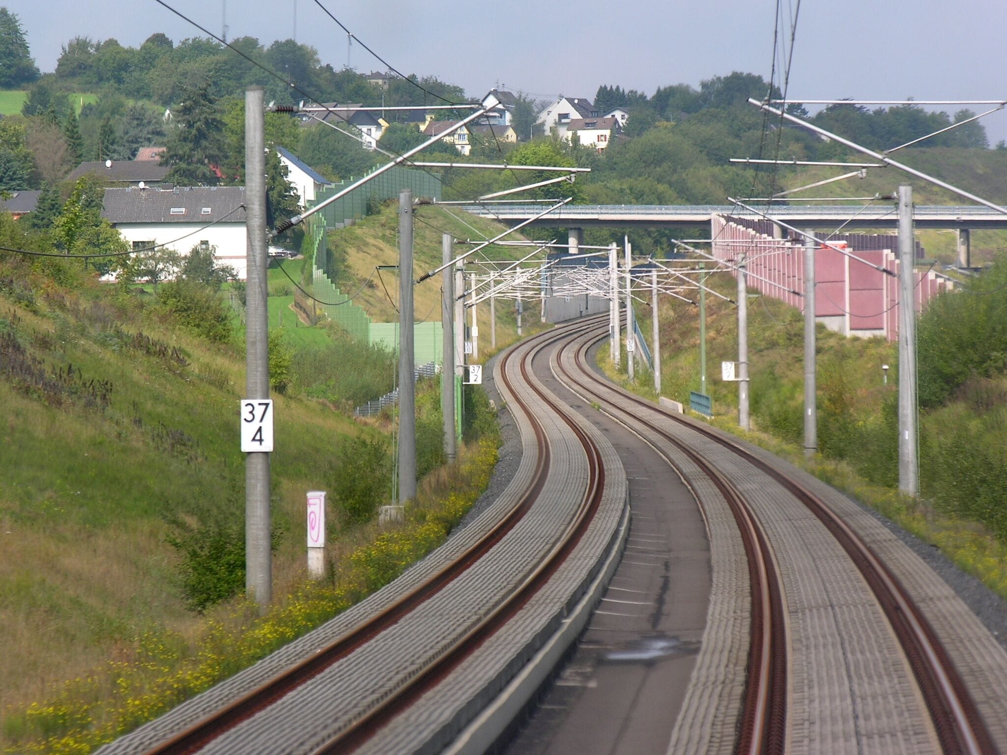Railway tracks curving through a hilly area with houses in the background.