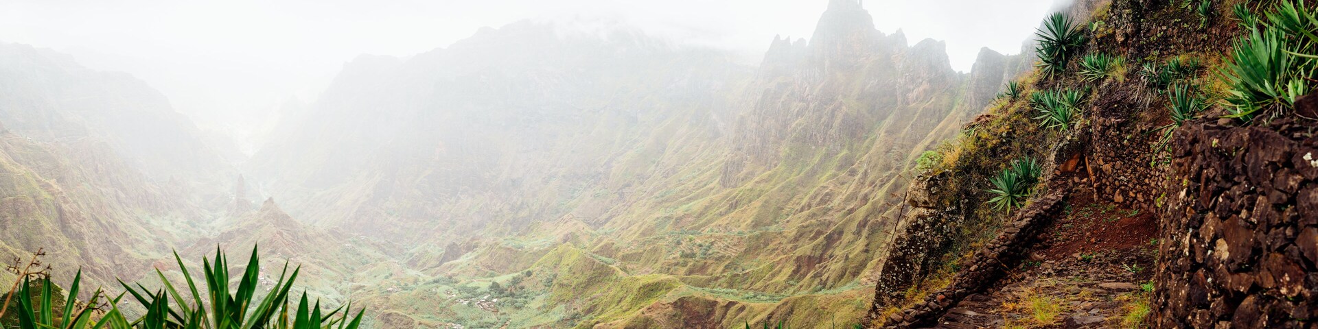 Paisagem montanhosa com um caminho estreito e vegetação verde.