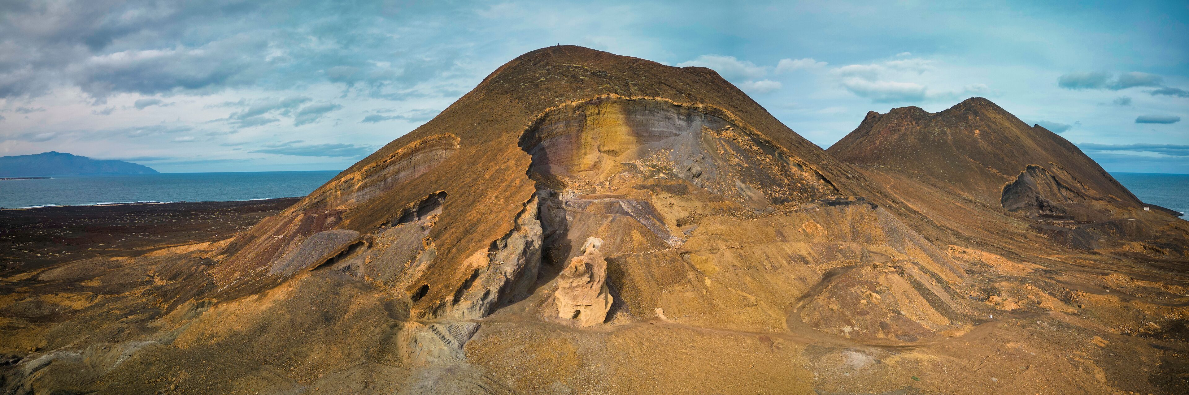 A rugged mountain landscape with a prominent peak and a coastal view.