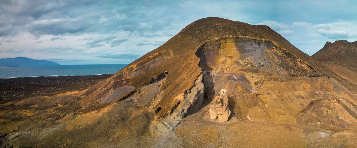 A rugged mountain landscape with a prominent peak and a coastal view.