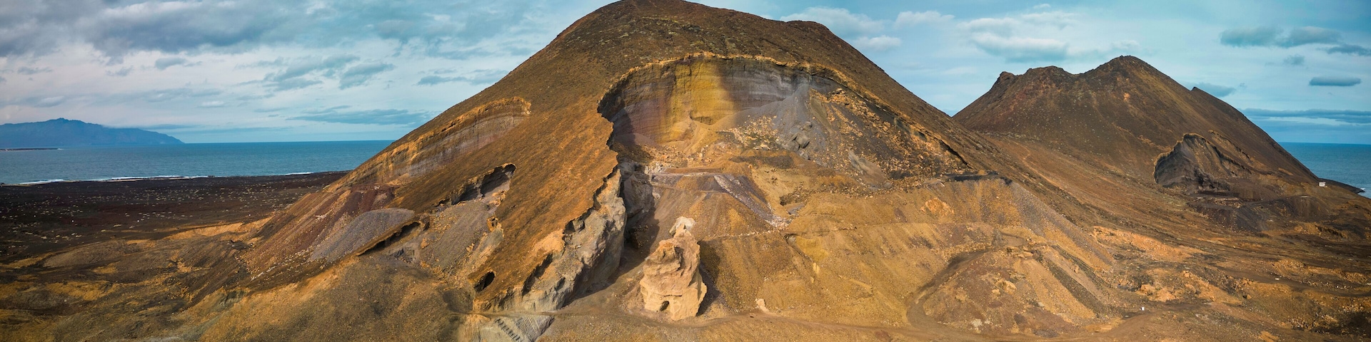 A rugged mountain landscape with a prominent peak and a coastal view.