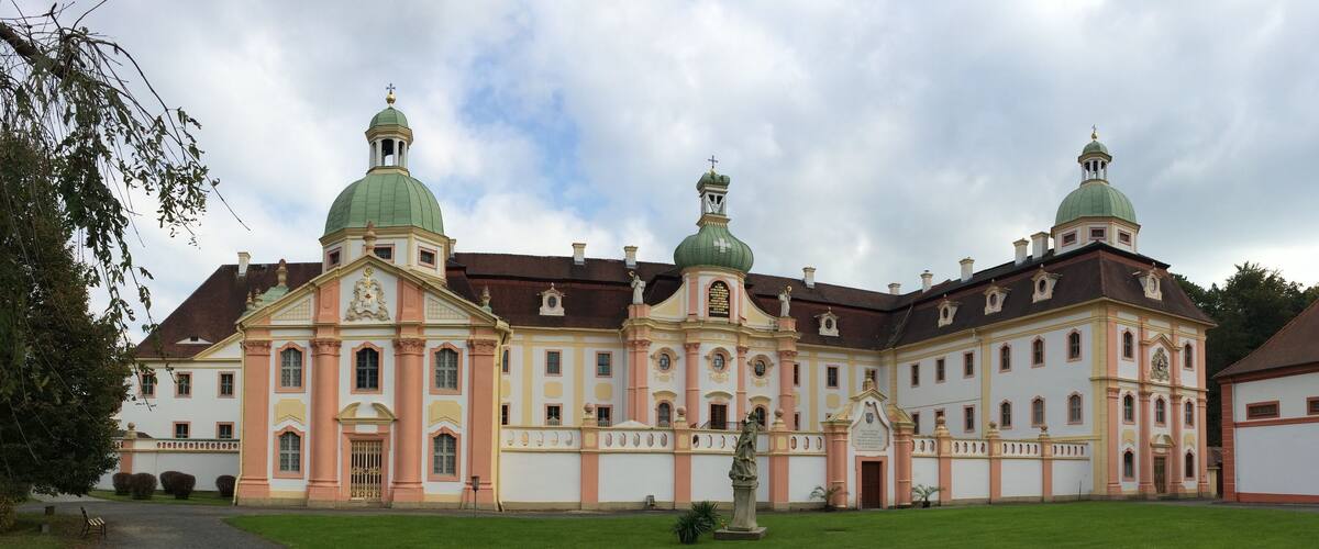A large, historic building with multiple domes and a statue in front.