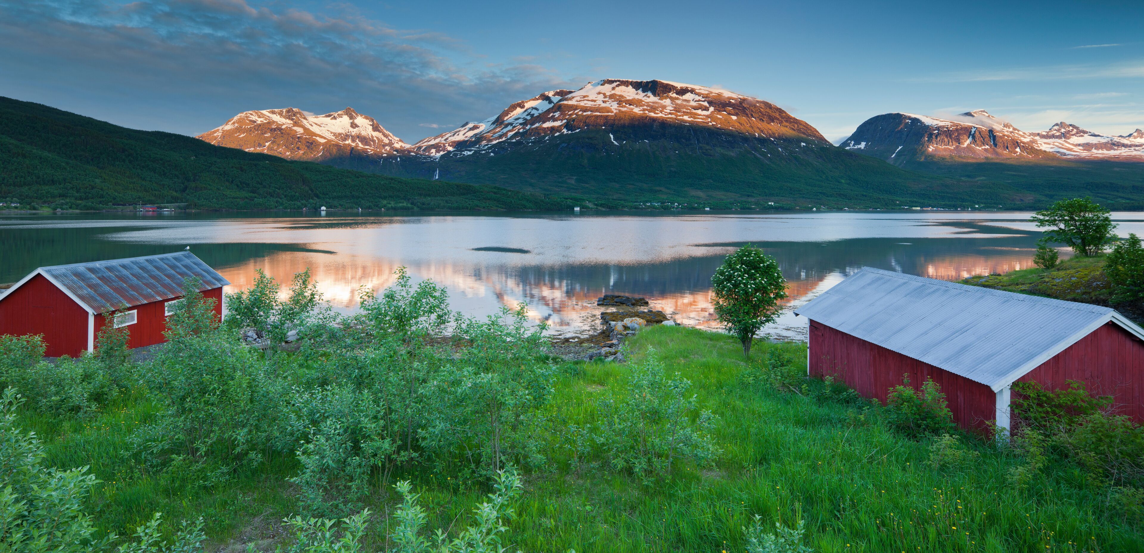 A serene lake with mountains in the background, surrounded by lush greenery and two red barns.