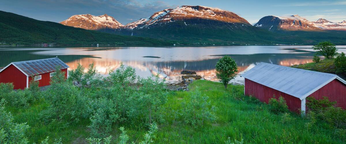 A serene lake with mountains in the background, surrounded by lush greenery and two red barns.