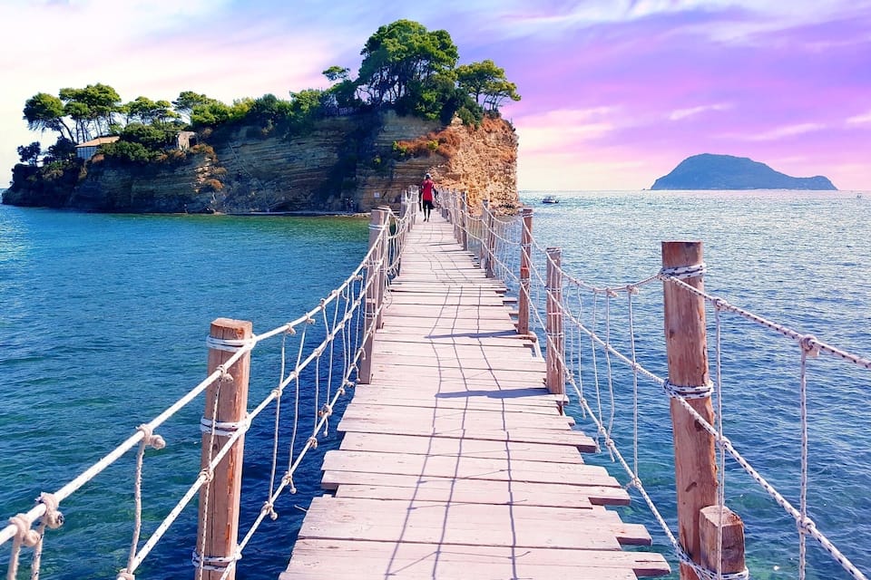 A wooden bridge over water with a rocky island in the background.