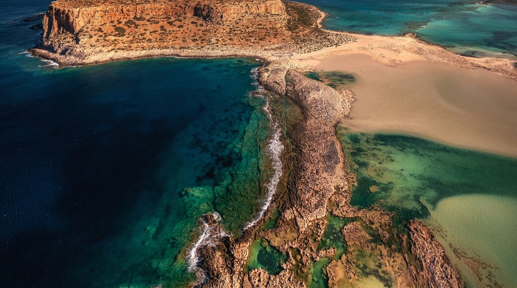 Majestic Morning at Balos, Crete: Serene turquoise waters caress the white sandy beach, embraced by dramatic cliffs under the golden morning sunlight