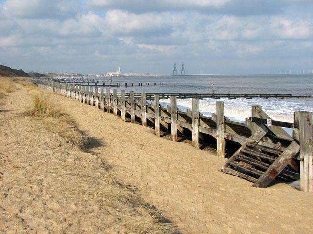 Groynes and revetment on the beach below Hopton-on-Sea. The Norfolk coastline is almost 100 miles long and extends from Hopton, just south of Great Yarmouth, northwards past the seaside resorts of Winterton, Happisburgh, Mundesley, Cromer, Sheringham and Holkham before it merges into Lincolnshire at King's Lynn. After the devastating floods in 1953, where 300 people lost their lives, the first sea defences were built along the coastline and at first the rate of erosion decreased. However, large portions of the revetments have been destroyed during the last 40 years, despite repairs, and beach and cliff erosion continue. The Shoreline Management Plan in its present format proposes no active intervention for a number of villages along the East Anglian coast, leaving them unprotected. One of these villages is Hopton, situated several miles south of Great Yarmouth, where the southern end of the Hopton to Corton seawall had to be closed due to storm damage, with the anticipation of a collapse of the structure > 1717919. A warning for walkers to take extra care has also been placed at the clifftop path > 1717876 where cliff falls on the path to Corton have occurred recently and more are expected > 1717883. Some blame the existence of the new outer harbour in Great Yarmouth for the loss of sand and beach area, and although some of the sand has since returned it is still at a low level. The privately owned East Port at Great Yarmouth, a multi-purpose facility integrating a new deep-water outer harbour, was opened in May 2007.