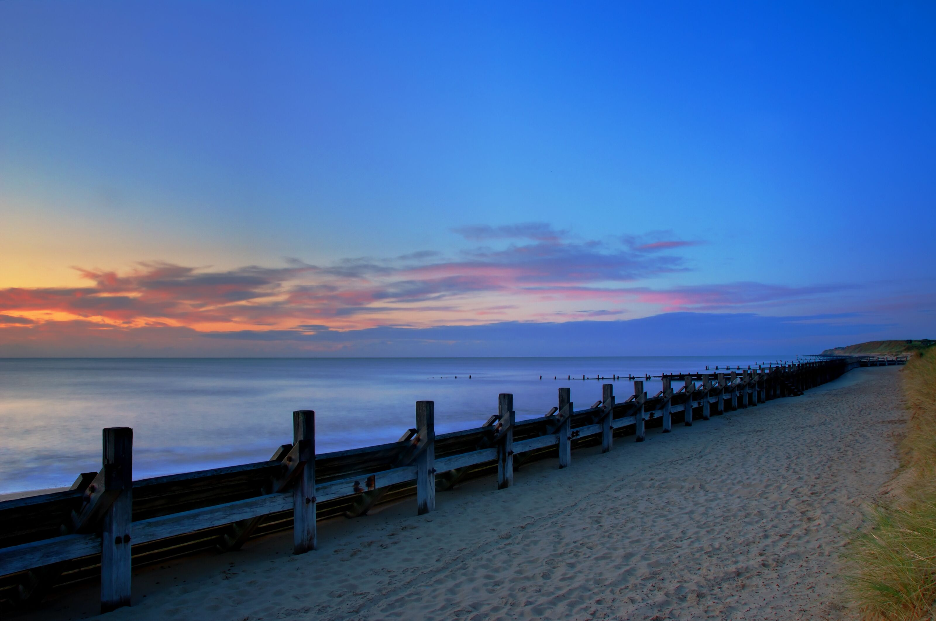 A beach with a wooden boardwalk extending into the ocean at sunset.