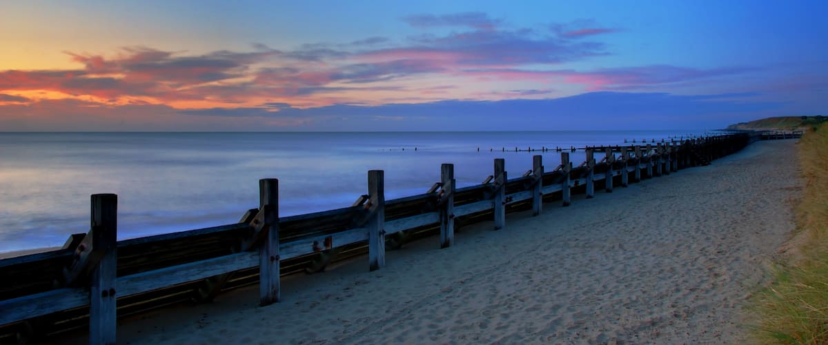 A beach with a wooden boardwalk extending into the ocean at sunset.