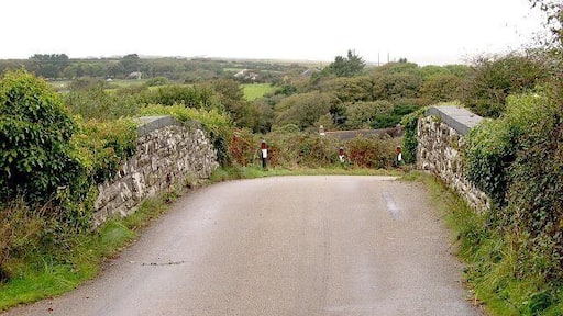 Bridge over the dismantled railway line at Mithian. This bridge used to carry the road from Mithian Down to Mithian over the Perranporth Railway branch line. The line has been closed for many years. Over the bridge is the land around the village of Mithian. The village itself is behind the trees on the right hand side of the picture.