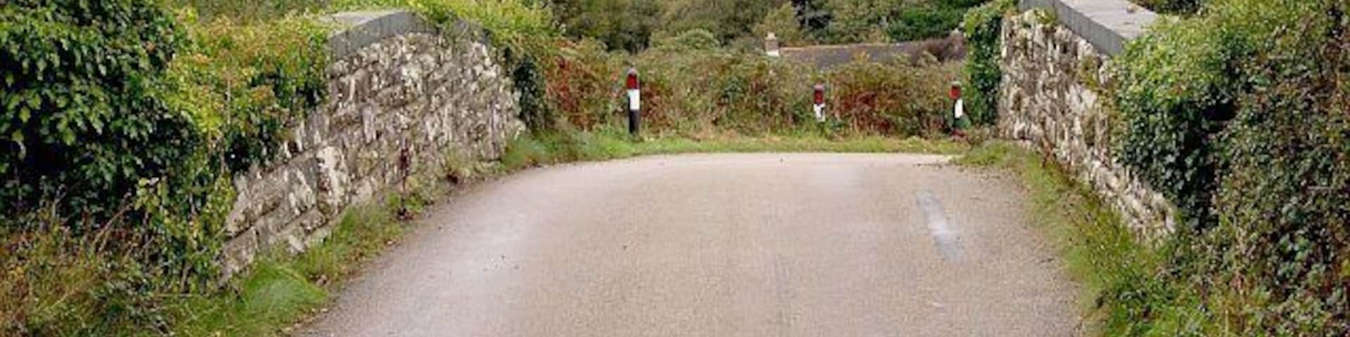 Bridge over the dismantled railway line at Mithian. This bridge used to carry the road from Mithian Down to Mithian over the Perranporth Railway branch line. The line has been closed for many years. Over the bridge is the land around the village of Mithian. The village itself is behind the trees on the right hand side of the picture.