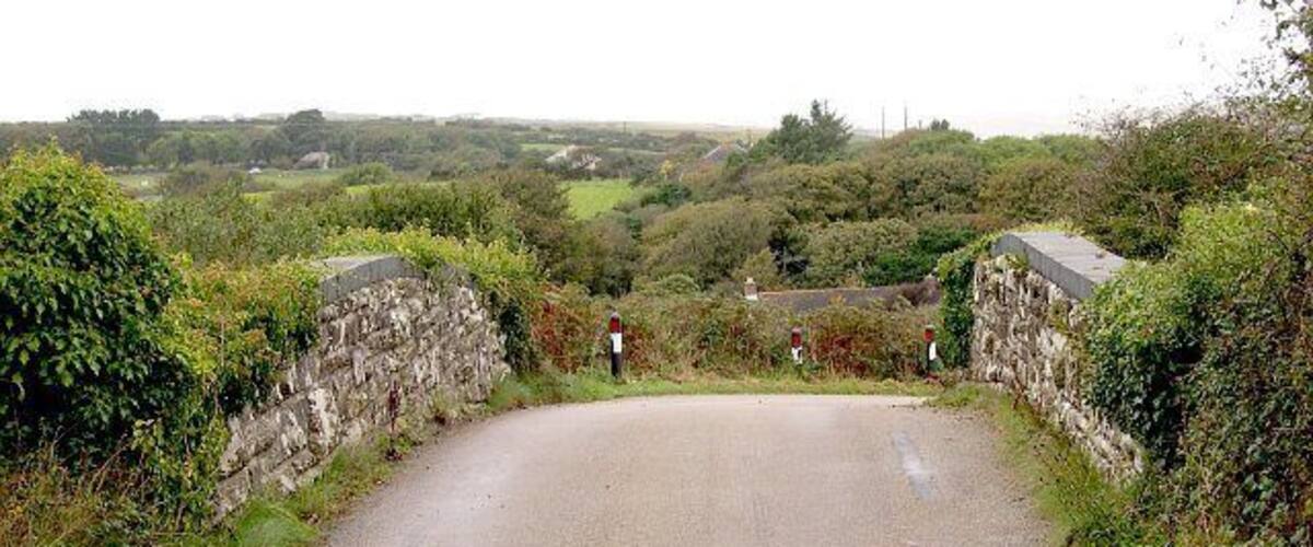 A narrow rural road flanked by stone walls and lush greenery.