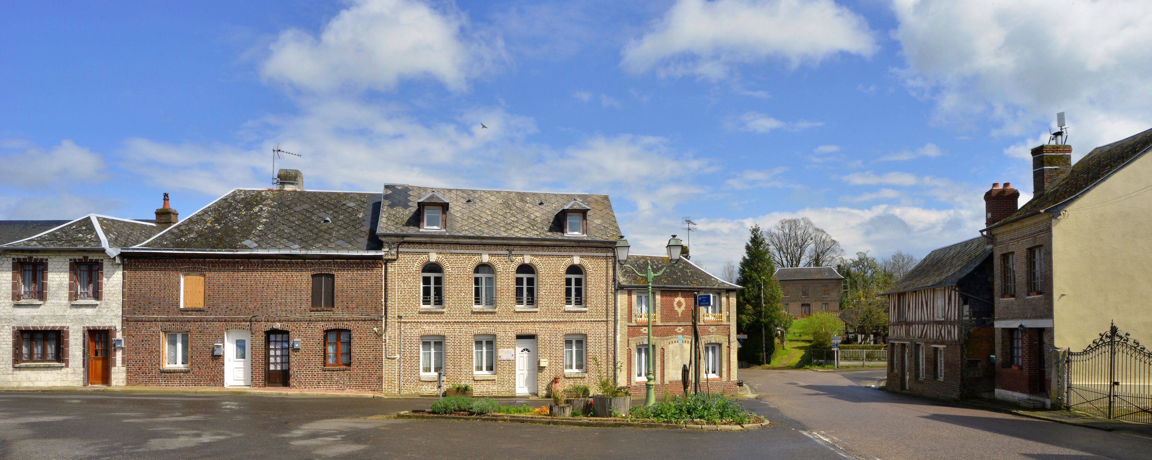 A quaint village street lined with historic buildings, including a prominent brick house with a gabled roof and a smaller adjacent structure with a tiled roof.