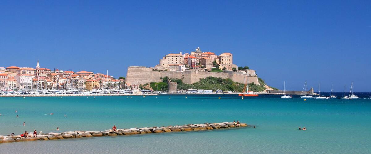 A coastal town with a historic castle on a hill, clear blue waters, and a rocky breakwater.