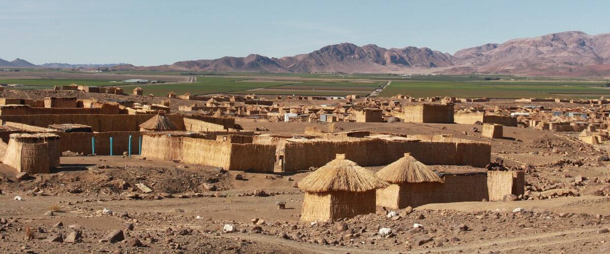 A desert village with thatched-roof houses and mountains in the background.
