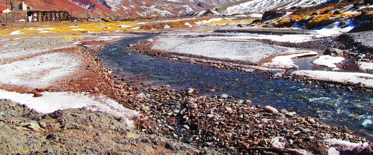 A river flowing through a mountainous landscape with snow-capped peaks and a clear blue sky.