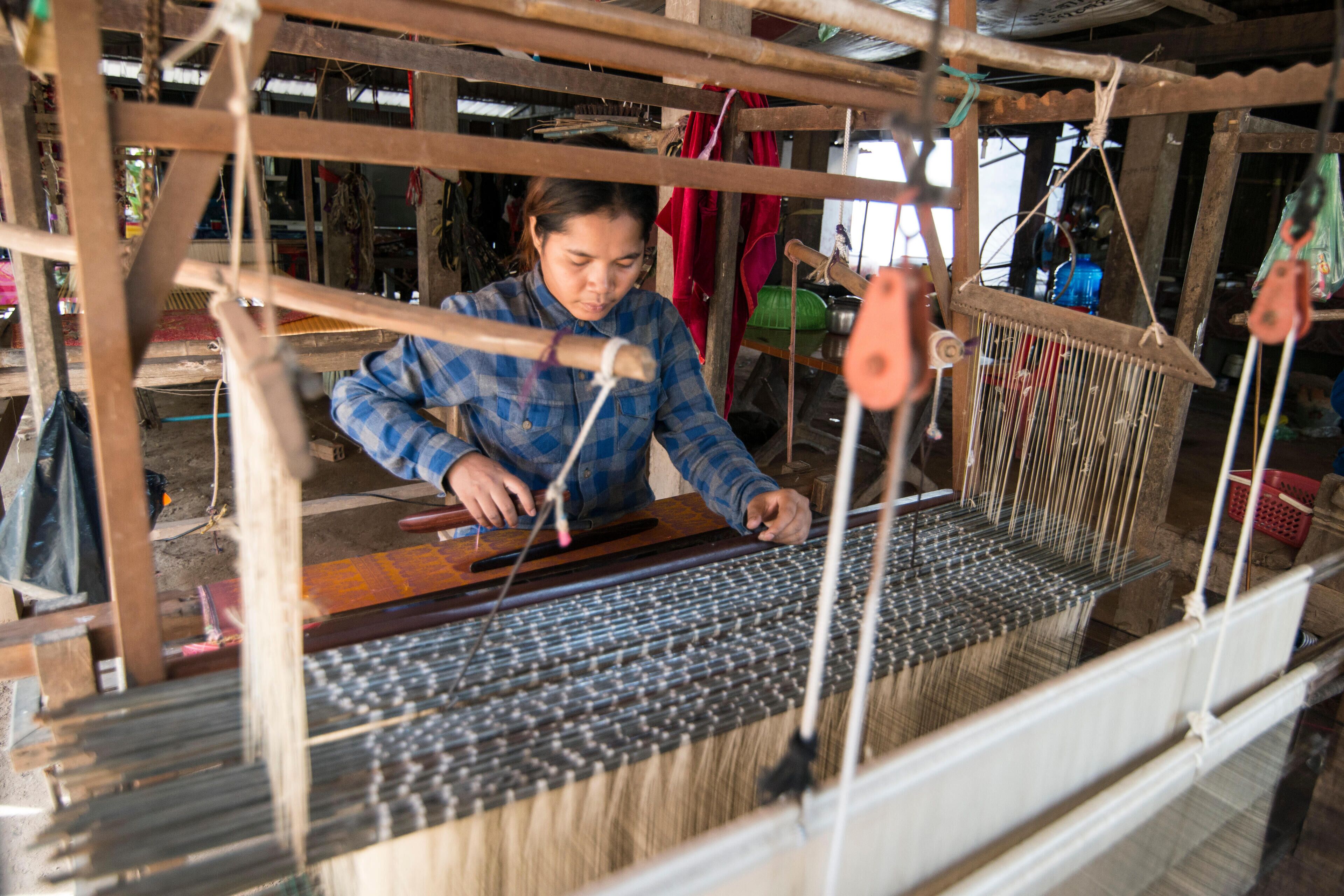 A person weaving on a loom in a rustic workshop.