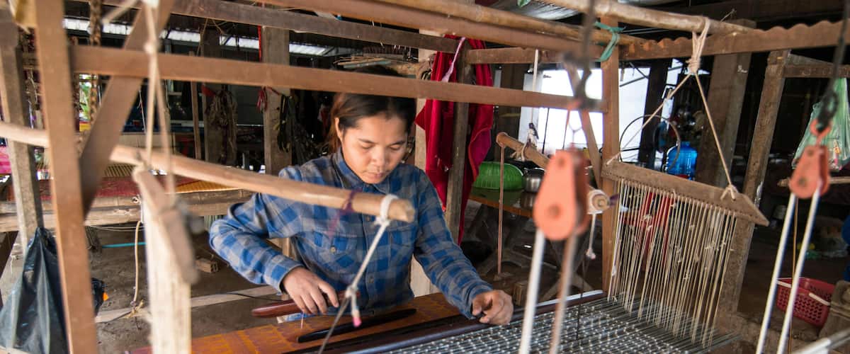 A person weaving on a loom in a rustic workshop.