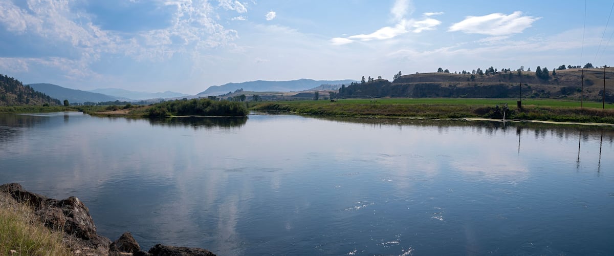 A calm river with a forested hillside and distant mountains.