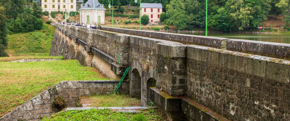 A stone bridge over a river, surrounded by lush greenery and historic buildings.