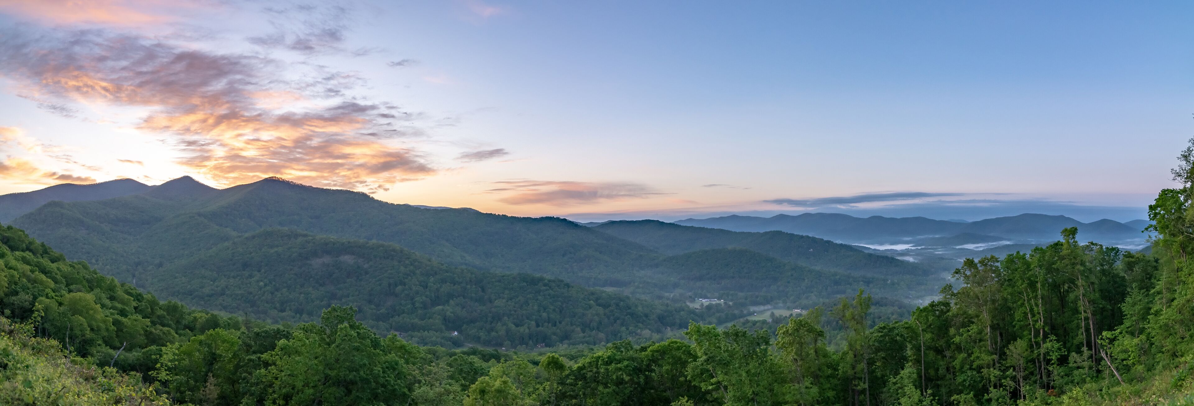 A mountainous landscape with dense forests and a sunset.