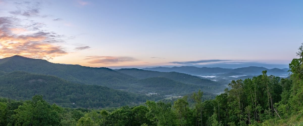 A mountainous landscape with dense forests and a sunset.