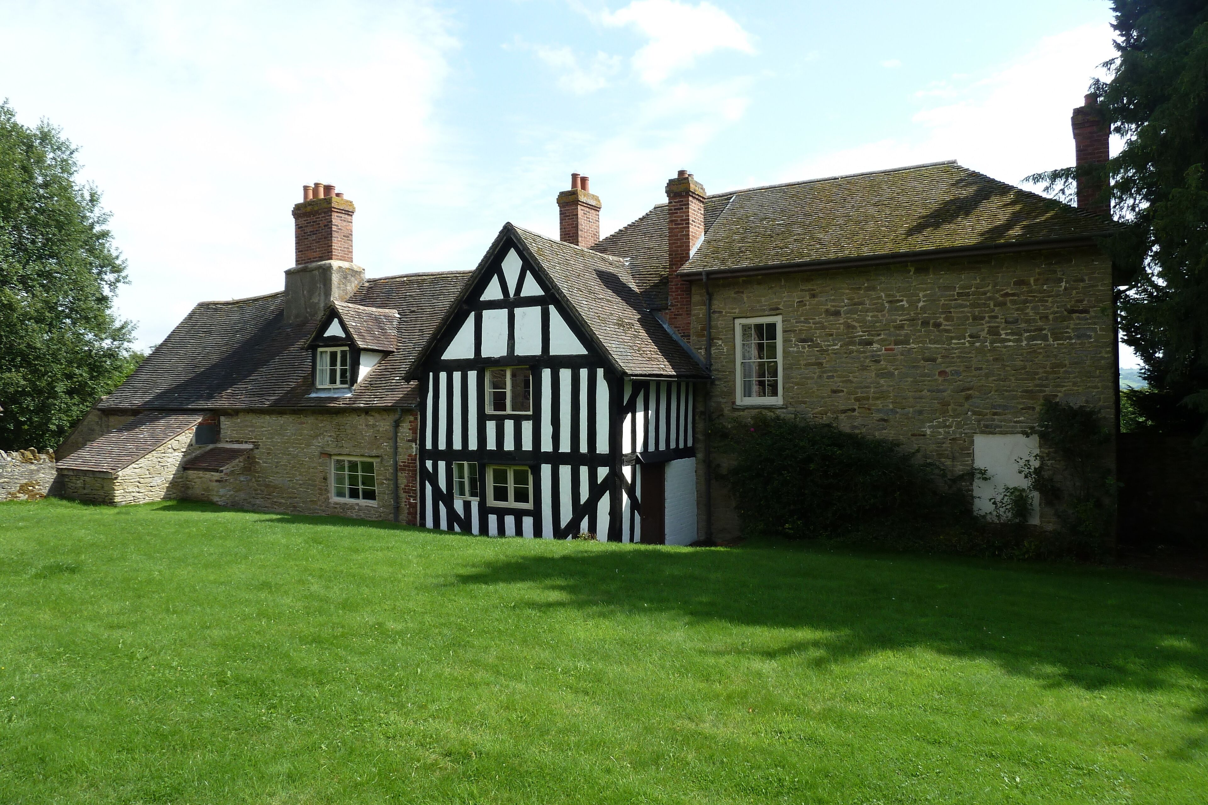 A Tudor-style house with a steeply pitched roof, multiple chimneys, and a well-maintained lawn.
