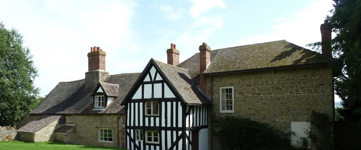 A Tudor-style house with a steeply pitched roof, multiple chimneys, and a well-maintained lawn.