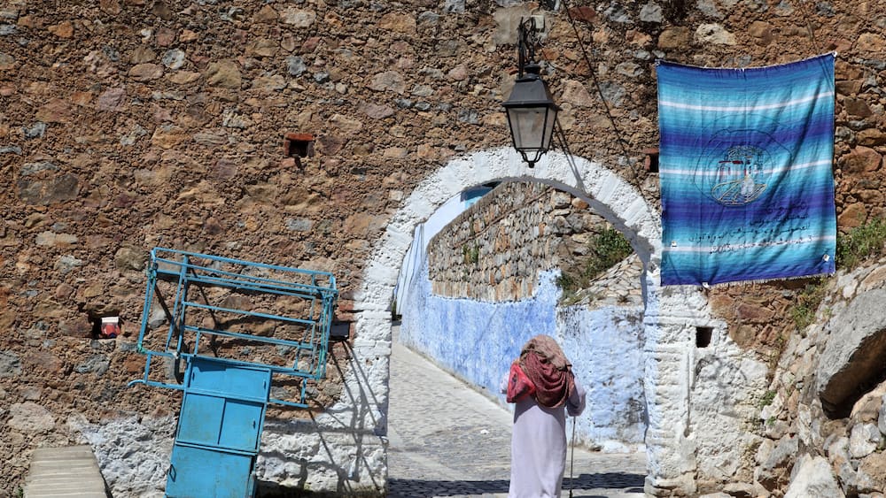 A stone wall, a blue metal structure, and a person walking.