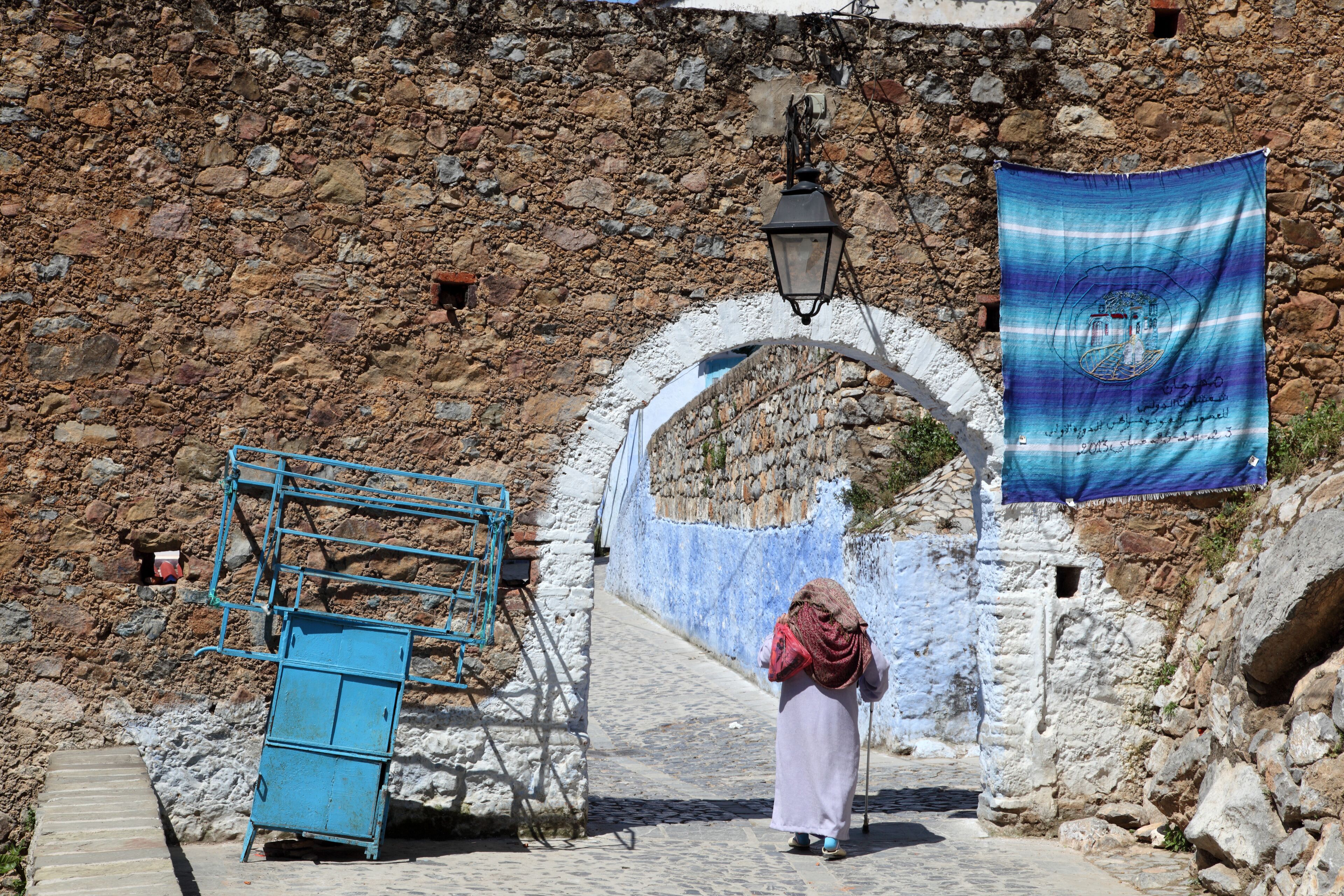A stone wall, a blue metal structure, and a person walking.