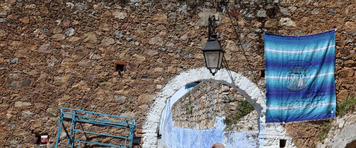 A stone wall, a blue metal structure, and a person walking.