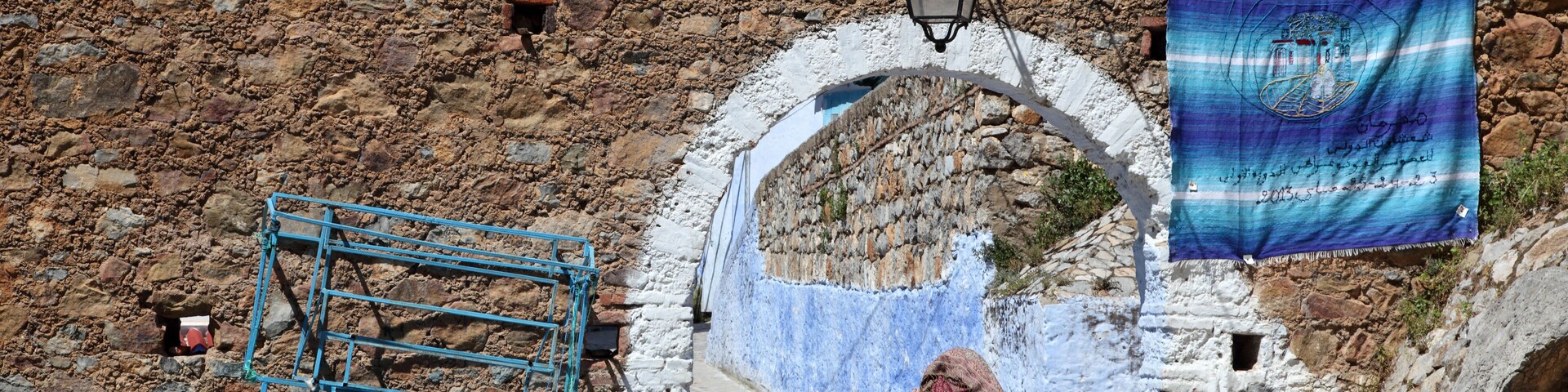 A stone wall, a blue metal structure, and a person walking.