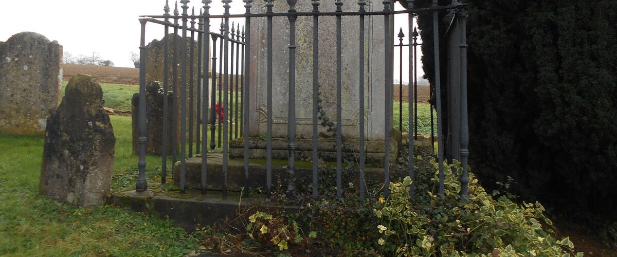 A cemetery with a gravestone enclosure and a large tree.